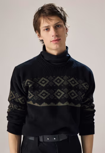 A man wearing a navy blue turtleneck sweatshirt with the sleeves rolled up