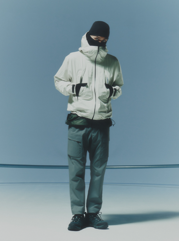 A man waring a white Goldwin jacket, grey pants and a black beanie along with black shoes and gloves