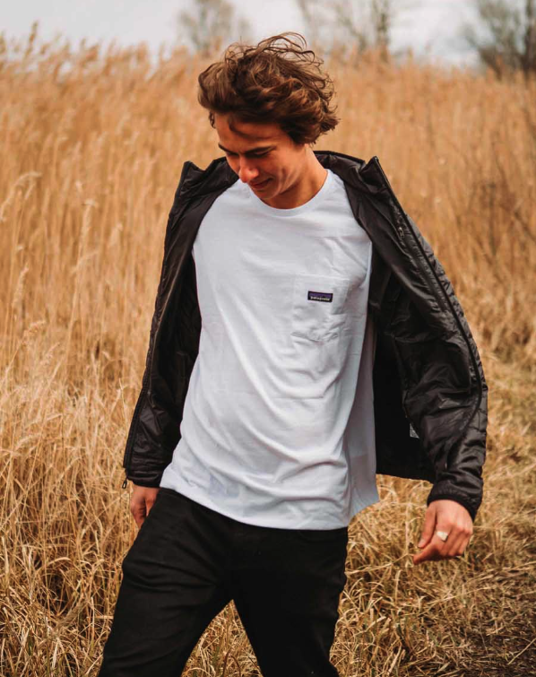 A man in a wheat field wearing a white Patagonia t-shirt along with black jacket and pants