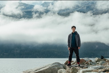 A man standing on rocks just off a lake wearing a Arc-teryx jacket, hoodie and pants