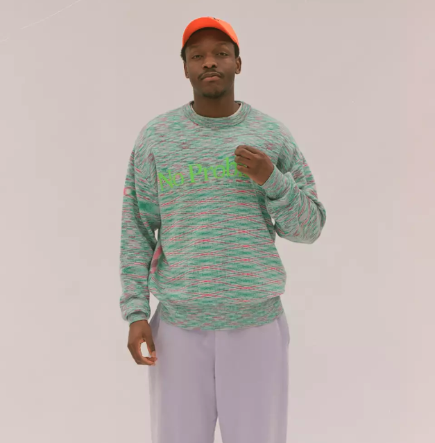 A man in a colorful Aries green sweater, lavender pants and an orange hat