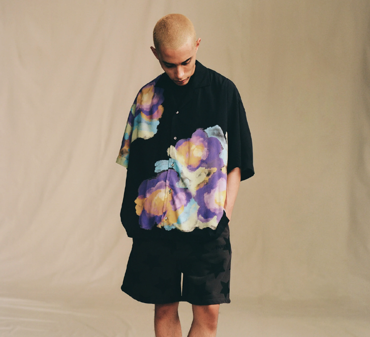 A man in a black Awake NY short-sleeve button up with a colorful floral print and black shorts