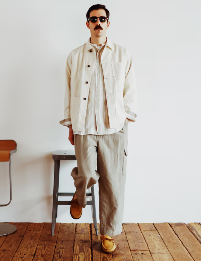 A man in sunglasses wearing a Beams Plus beige overshirt with oversized grey pants and brown shoes