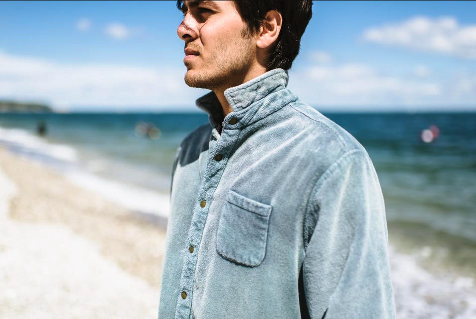 A man standing on the beach wearing an blue Adam Mar long-sleeve button up shirt