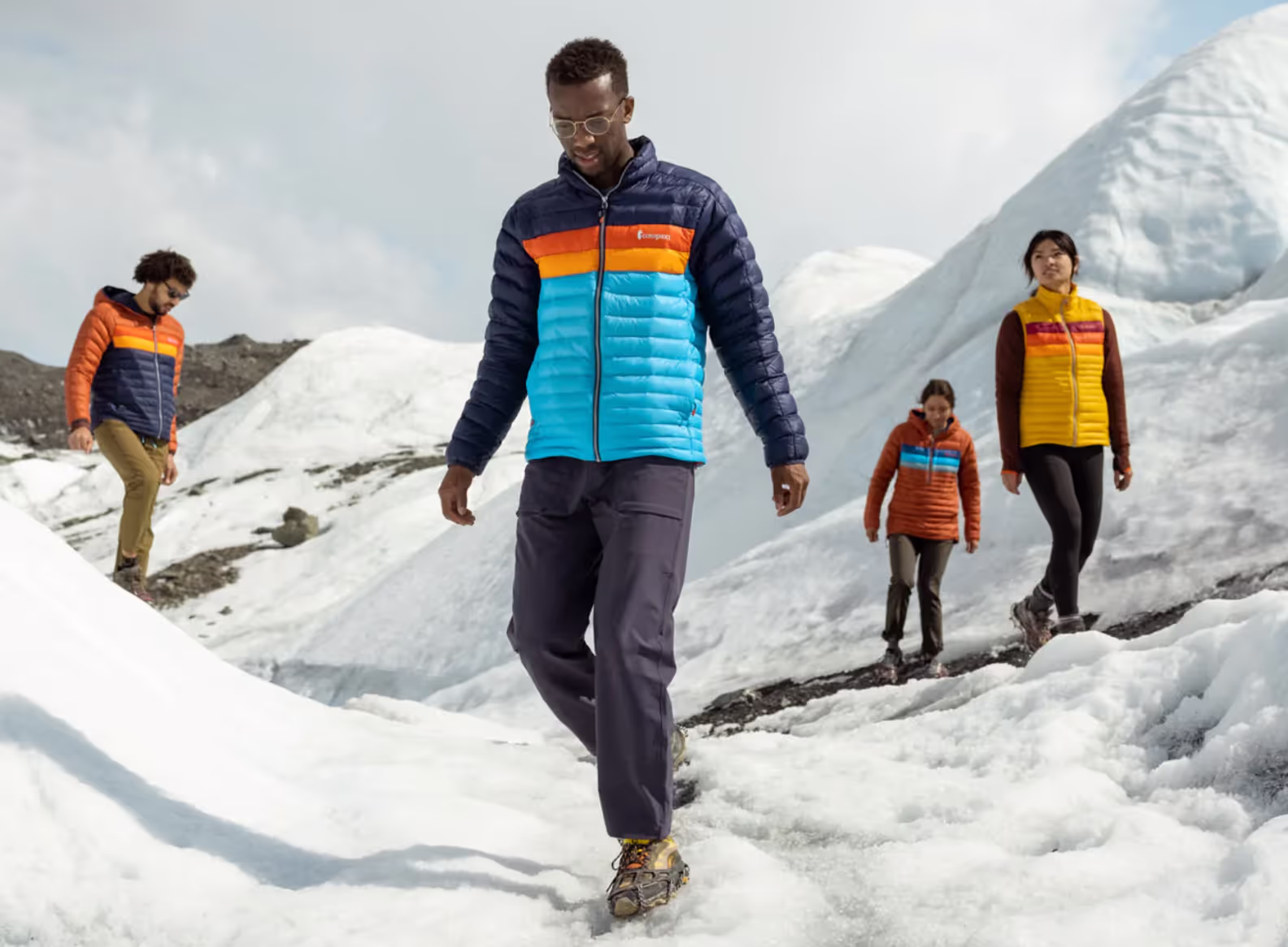 A group of people hiking on a snowy mountain wearing colorful CotoPaxi Puffy Jackets and active wear