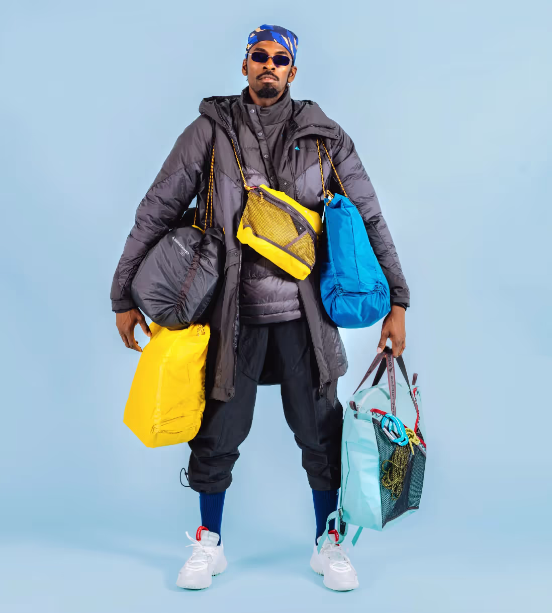 A stylish man wearing many layers of Klattermusen clothing including numerous jackets and bags