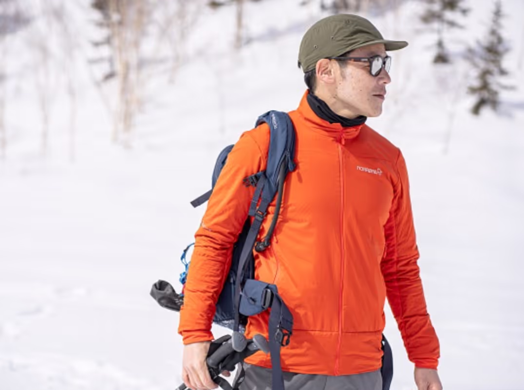 A man looking off in the distance on a snowy mountain wearing an orange Norrona jacket