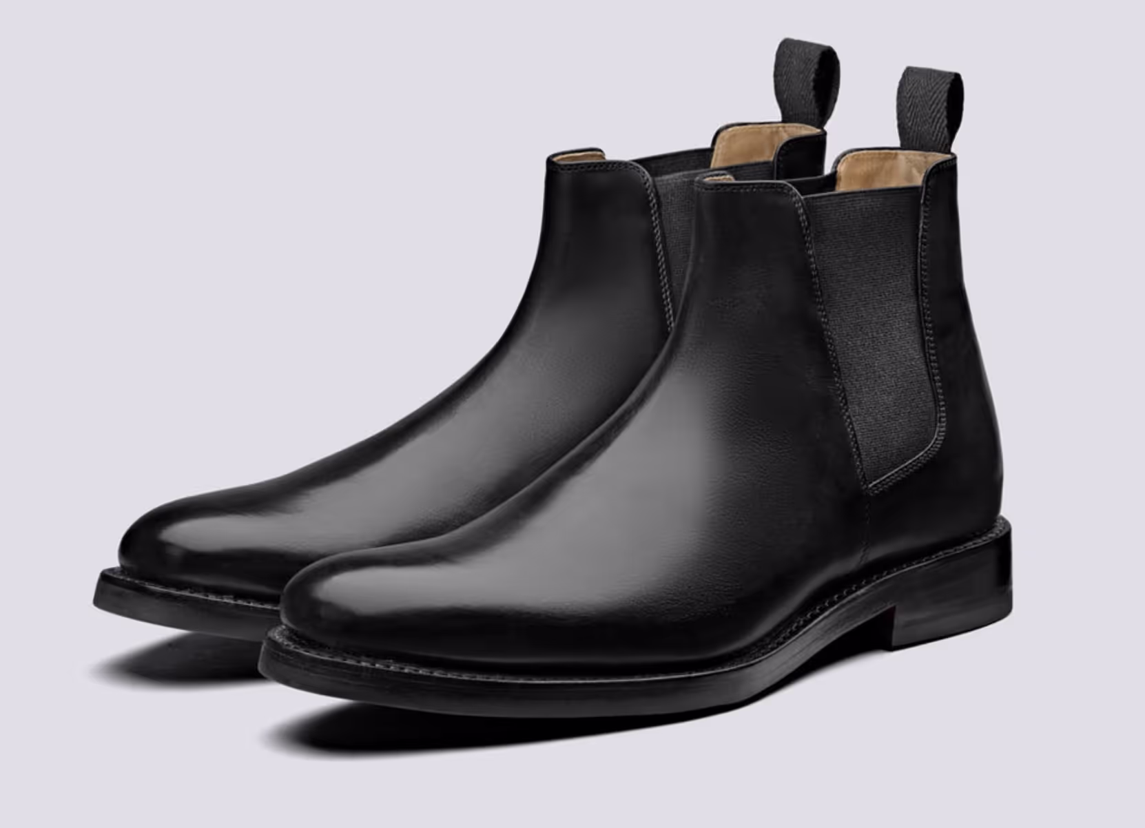 A black pair of Grenson boots that are similar to Blundstones on a white background