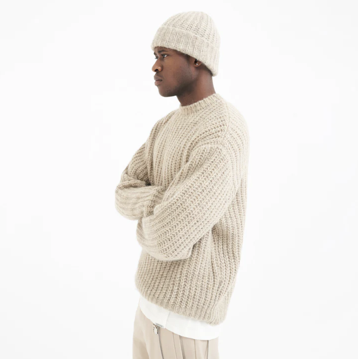 A man wearing a Represent beige knit sweater with a matching beanie and pants