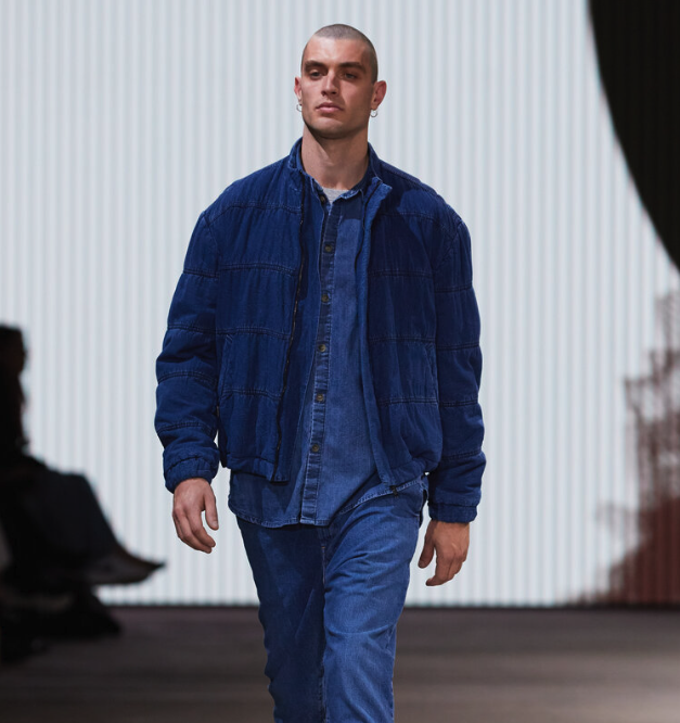 A man walking in a Bassike denim jacket with matching button up and pants