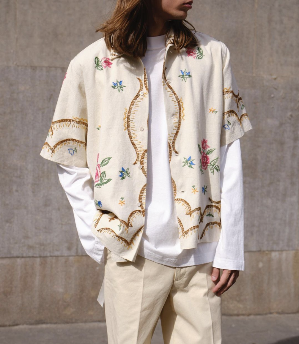 A man with long hair wearing a Damir Doma beige floral button up with biege pants and a white longsleeve