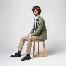 A man sitting and wearing an ISTO green jacket, beige pants and black shoes
