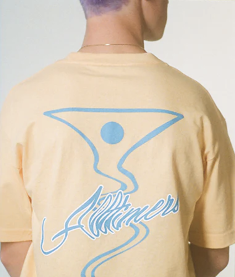A man wearing a peach and light blue All-timers t-shirt with a martini graphic on it