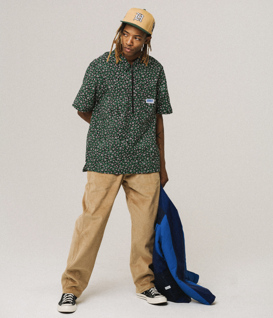 A man wearing a green floral The Hundreds short-sleeve button-up, khaki pants and a beige hat