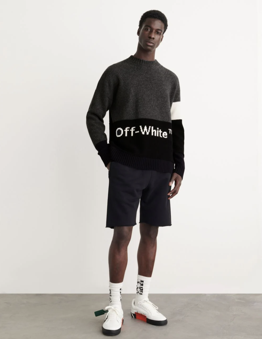 A man wearing a black Off-White sweater, black shorts and branded Off-white socks