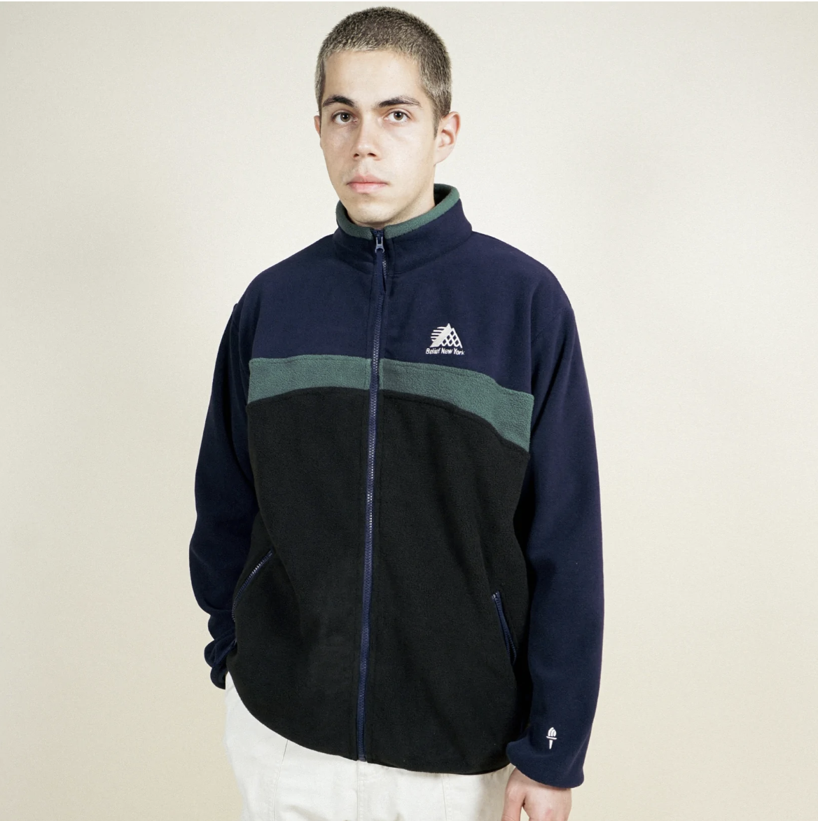 A man wearing a navy blue and green Belief fleece and white pants