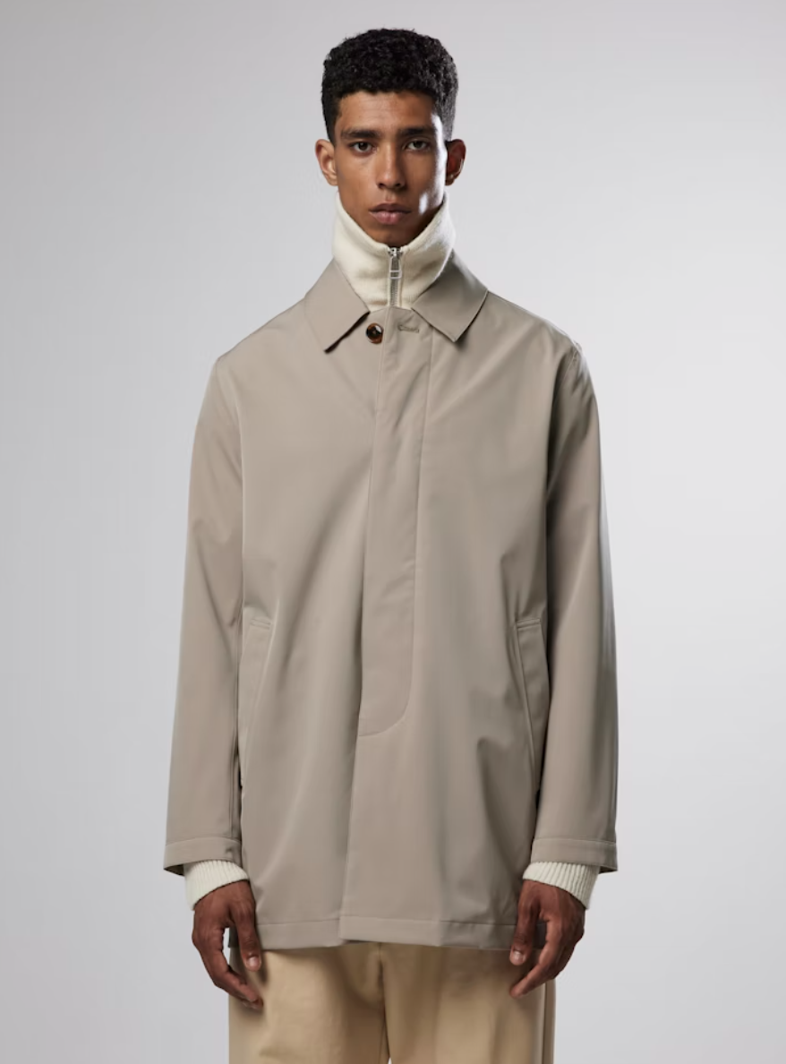 A man wearing a beige NN07 trench-coat with a beige turtle neck and brown pants