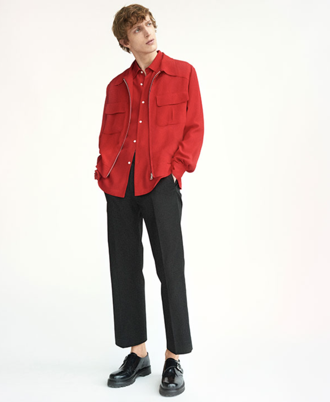 A man wearing a red Sandro button-up with a red over-jacket and black pleated pants