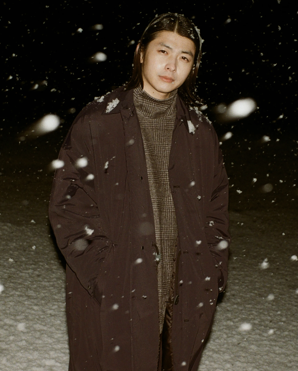 A man wearing a brown N. Hoolywood overcoat with a checkered plaid turtle neck