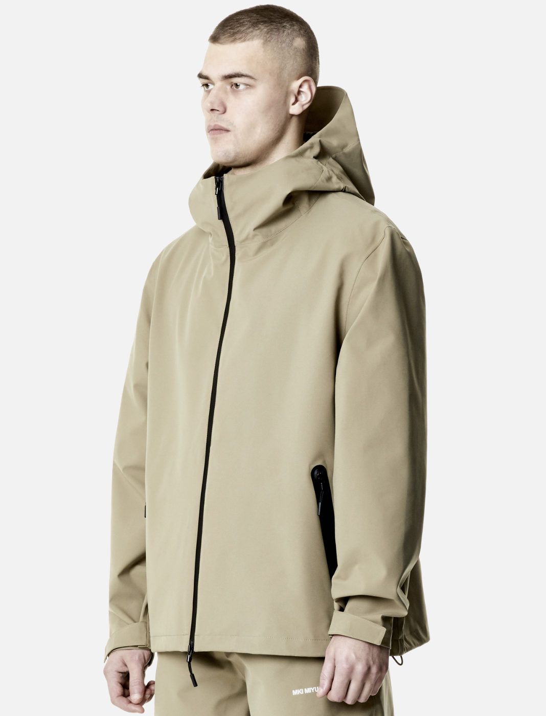 A man wearing a MKI Myuki beige technical jacket with matching pants