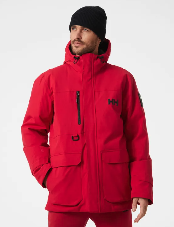 A man wearing a bright Red Helly Hanson winter Jacket with matching red pants and a black beanie