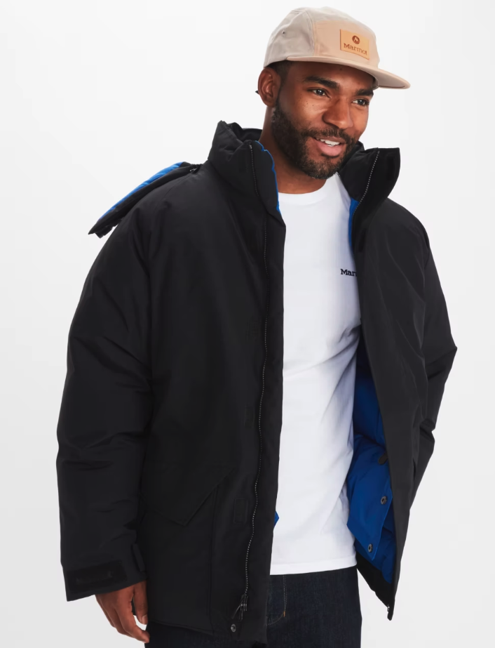 A man wearing a Marmot outfit feating a white t-shirt, black winter coat and a beige hat