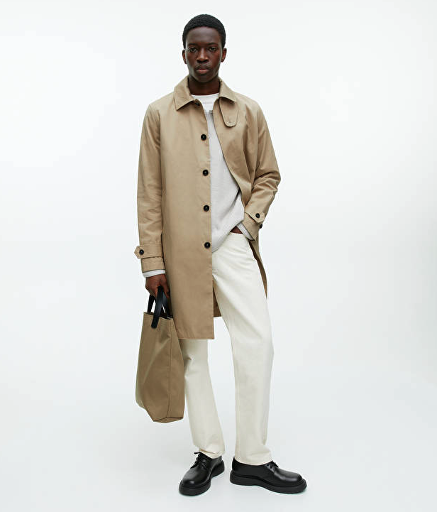 A man wearing a brown Arket trench coat and cream pants with black loafers