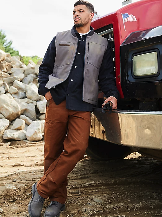 A man wearing a wrangler vest, button up and brown pants