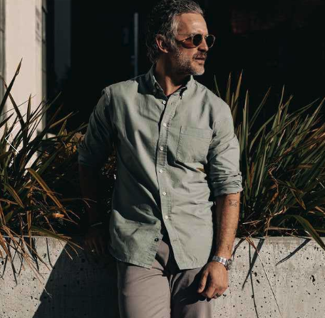A man wearing a Taylor Stitch olive long-sleeve button up, grey pants and sunglasses