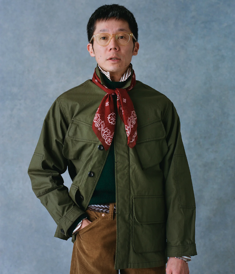 A man wearing a Drake's green coat, red bandana and brown pants
