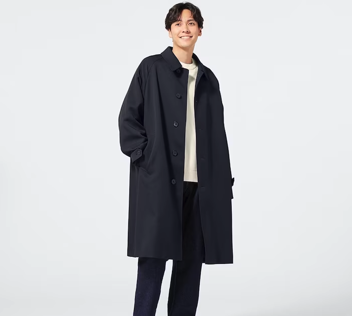 A man wearing a minamilist Gu navy blue overcoat, with a white shirt and navy blue pants