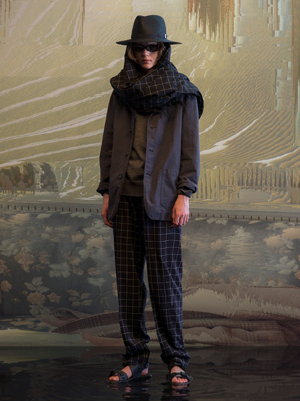 A man wearing a full Undercover outfit with a black jacket and black plaid pants with a matching scarf