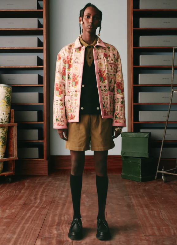 A man wearing a pink floral print Bode jacket, brown shorts and high black socks
