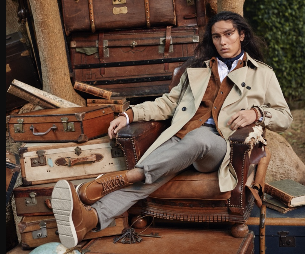 A man sitting in a chair wearing a Banana Republic trench coat, a brown jacket underneath and brown shoes