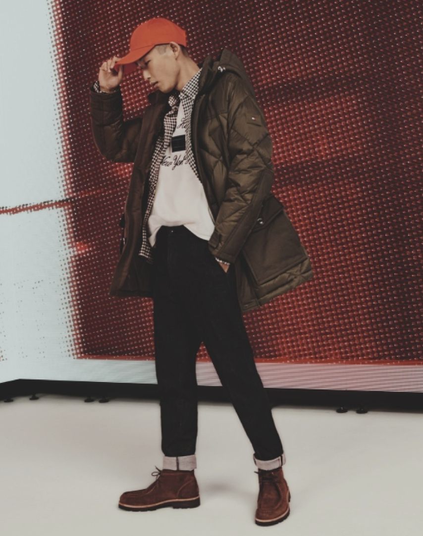 A man wearing a red Tommy Hilfiger hat, brown winter coat and jeans