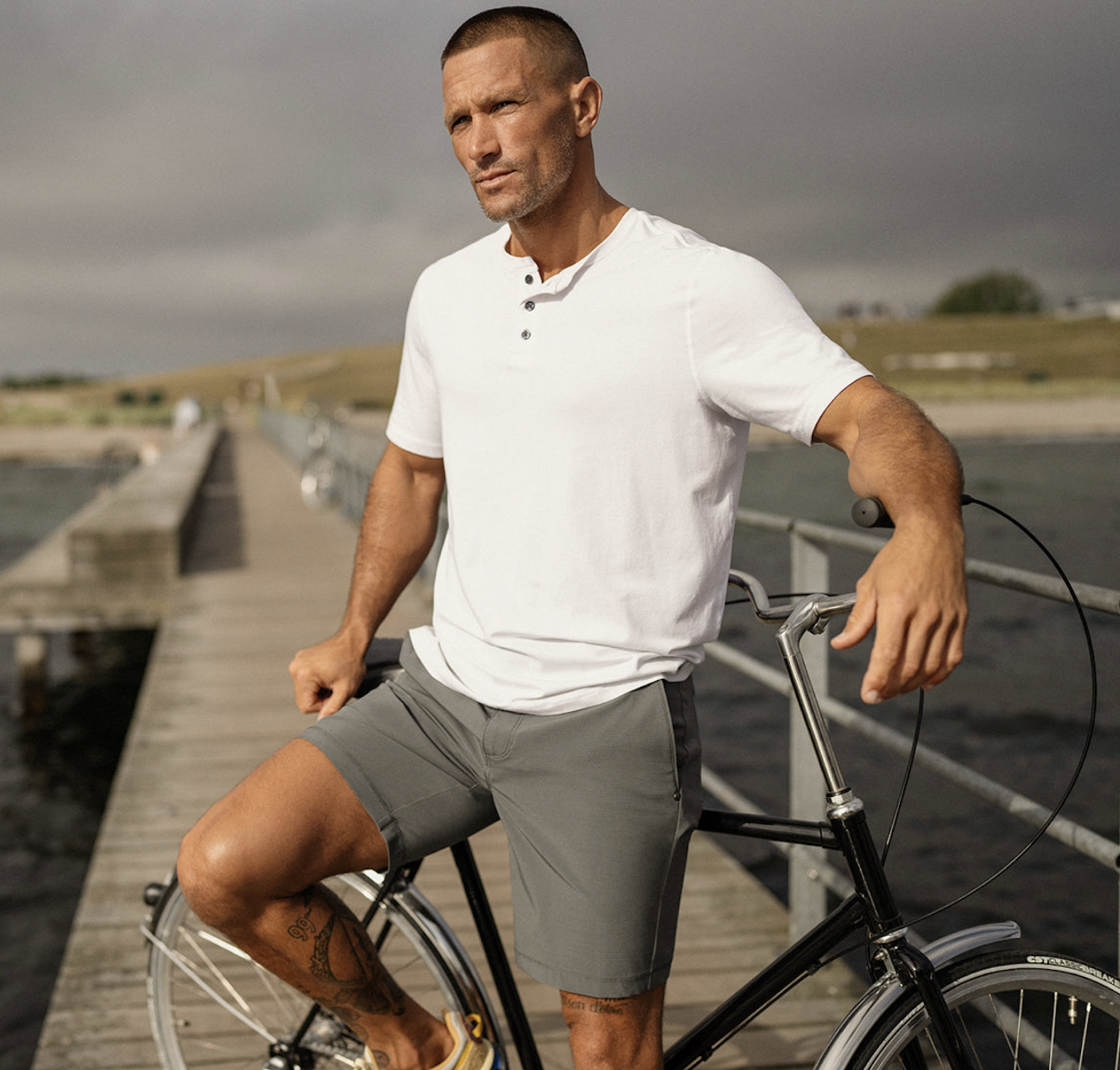A man wearing a Vuori outfit sitting on a bridge with a white shirt and dark grey shorts