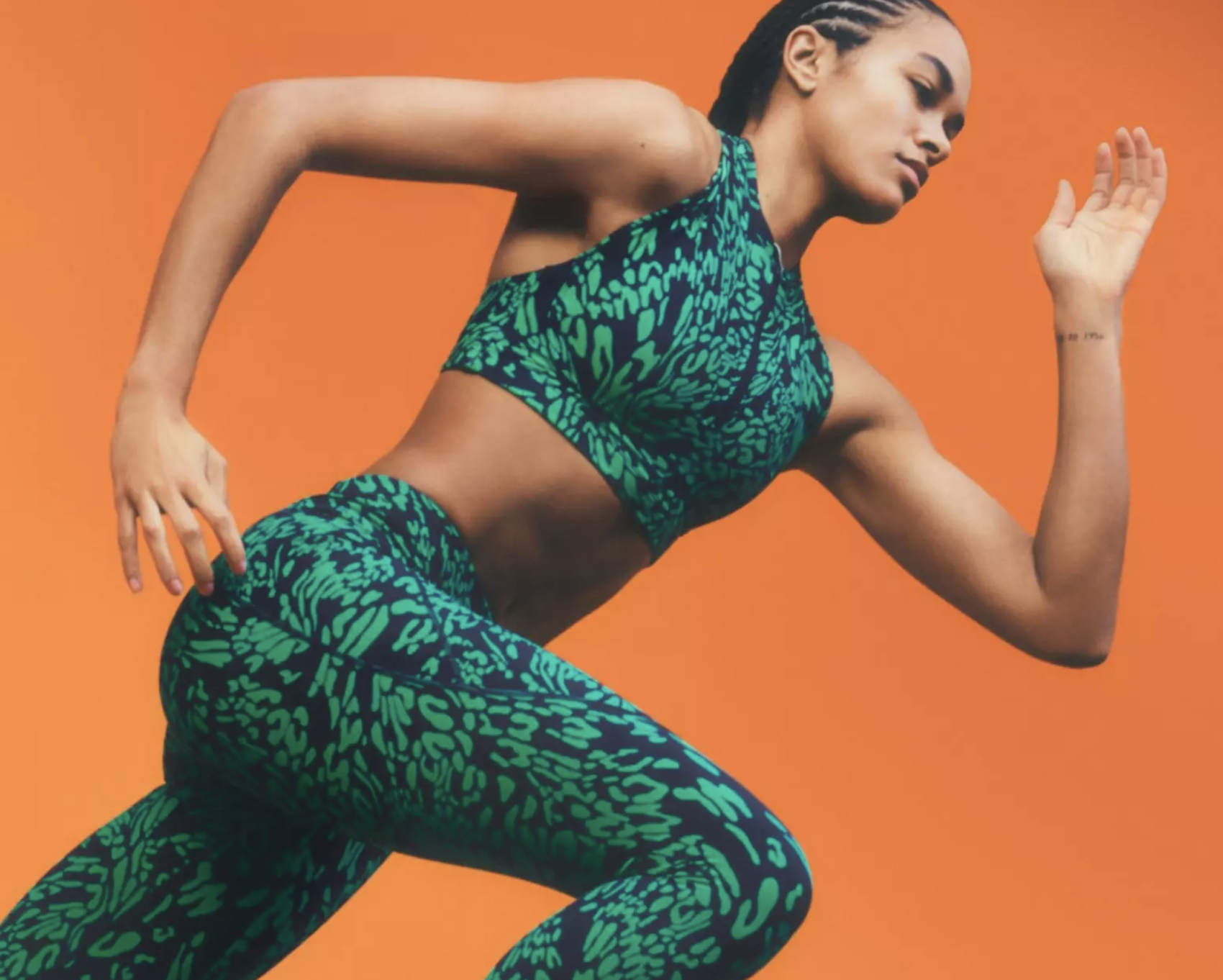 A woman mid-sprint wearing a colorful green Sweaty Betty athletic spandex