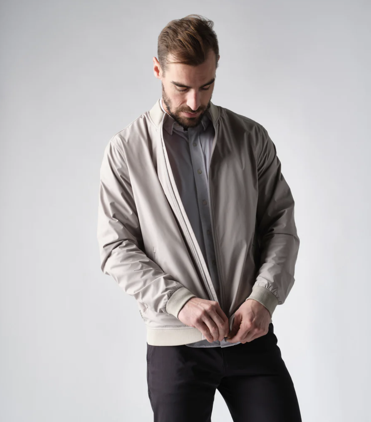 A man zipping up his Rhone coat overtop a grey button up