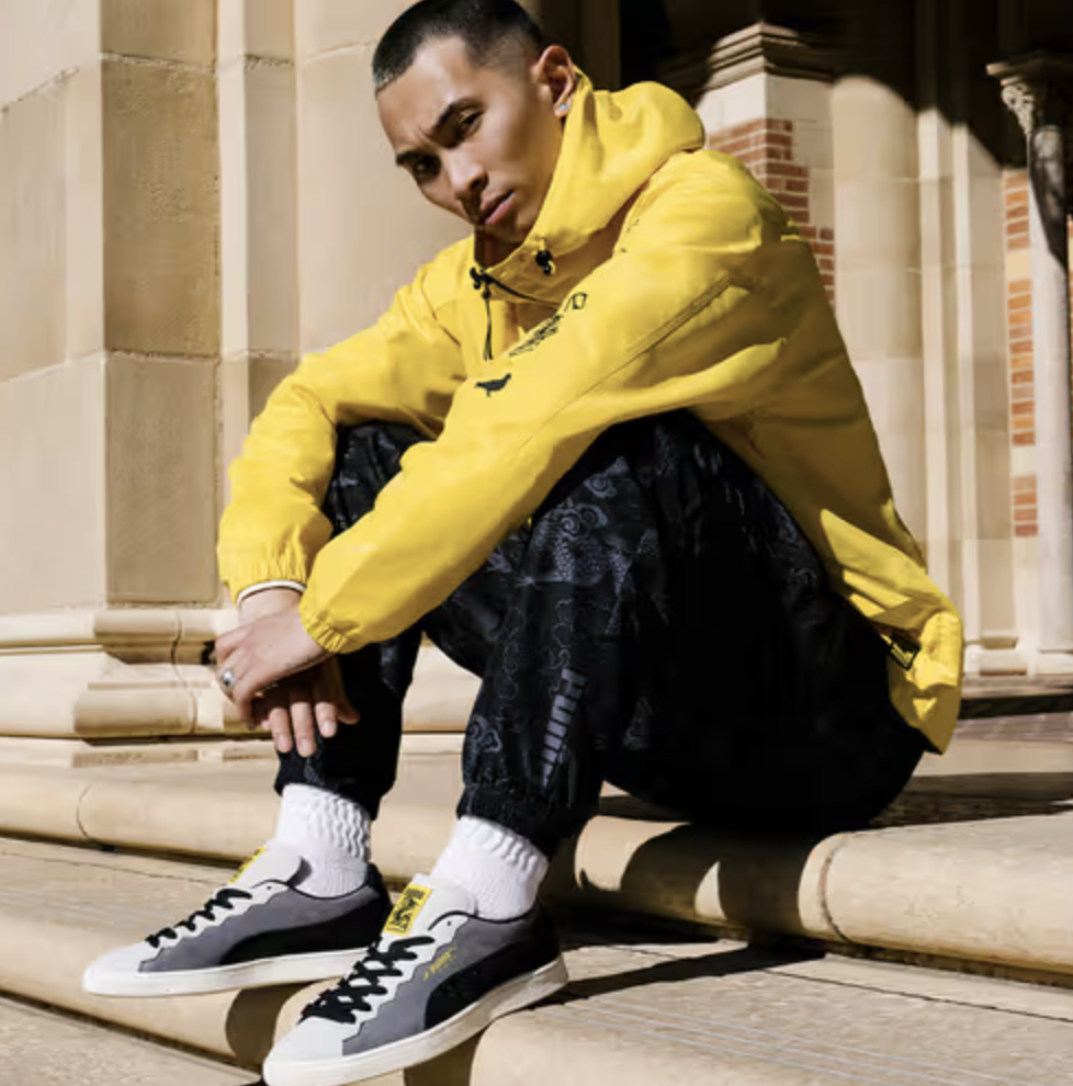 A man sitting on a city step wearing a Puma yellow outfit and matching sneakers