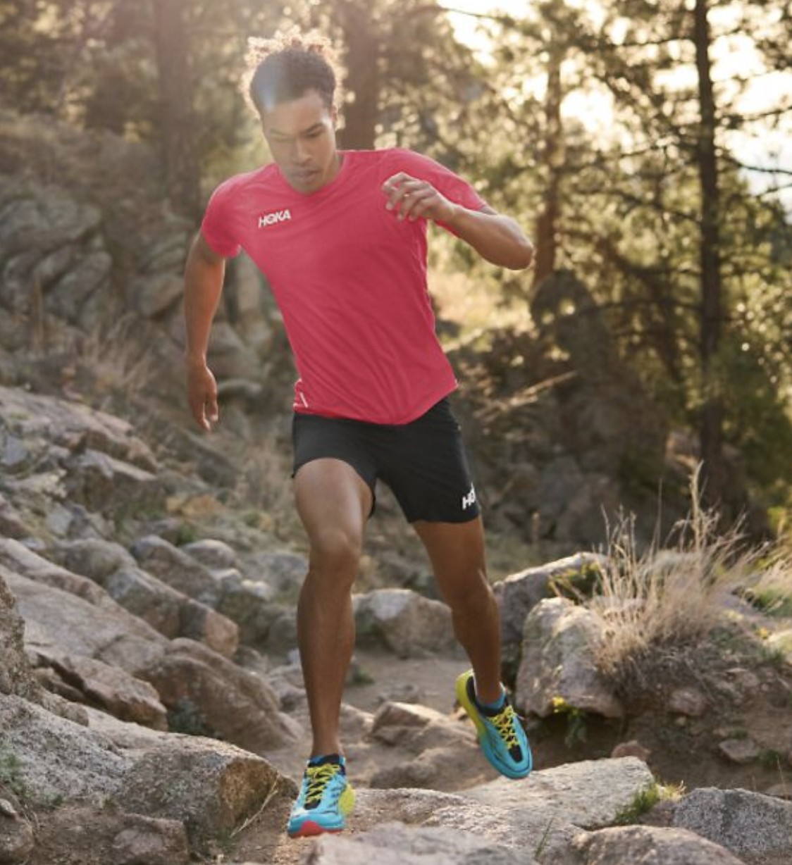 A man running in a Hoka One One outfit with a red shirt, black shorts and colorful sneakers