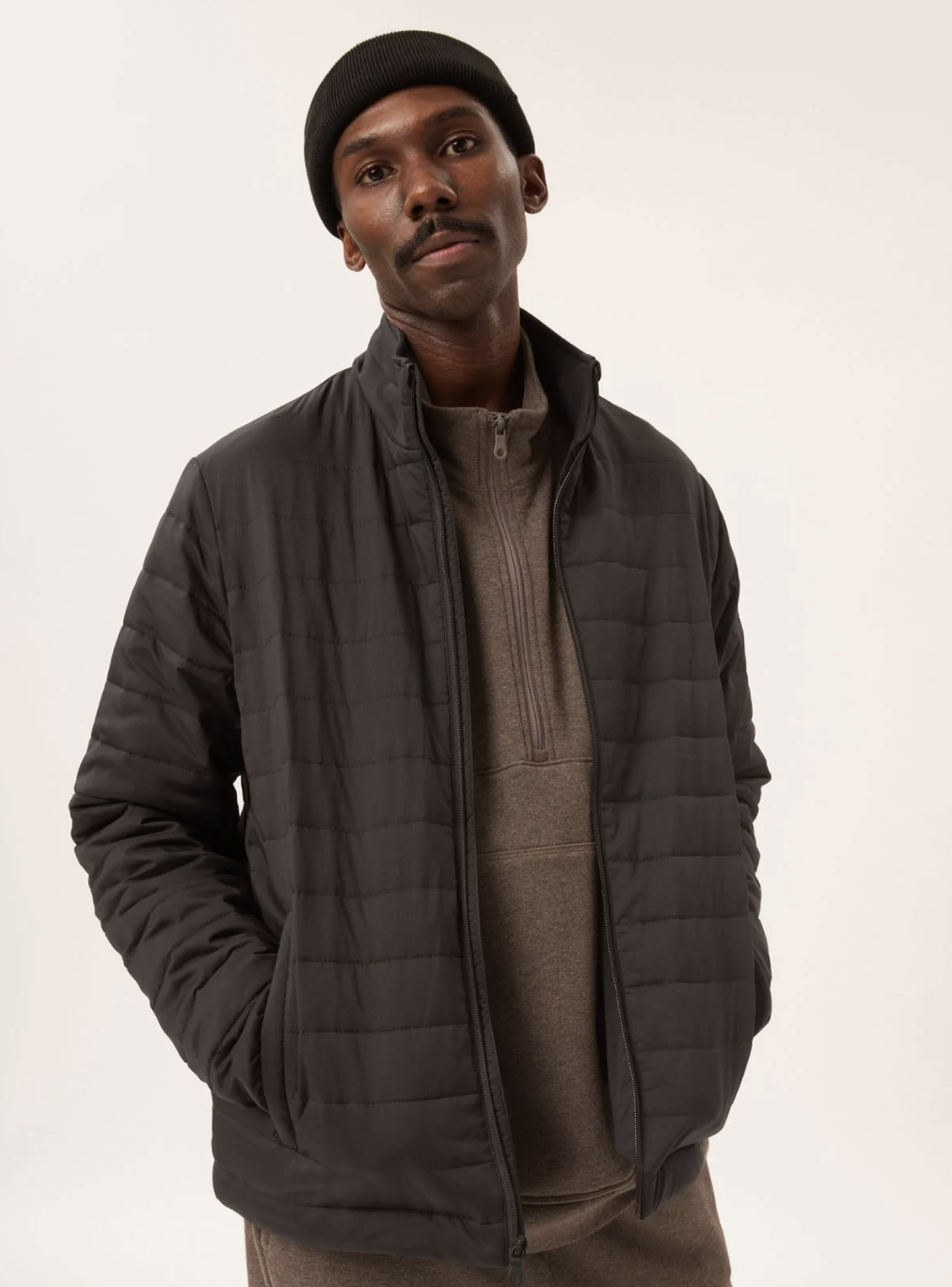 A man wearing a Girlfriend Collective puffy black coat with a black beanie