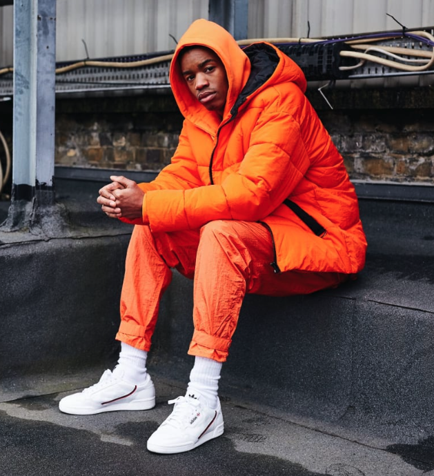 A man sitting in a bright orange Adidas tracksuit and white sneakers
