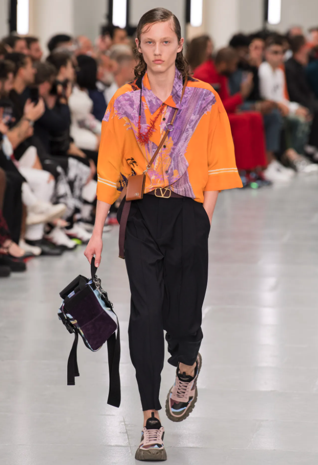 A person wearing an orange Valentino button up, black pants and colorful sneakers