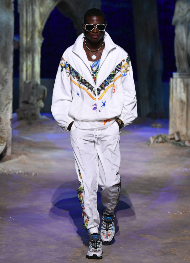 A man wearing a white Versace tracksuit with colorful print and matching sneakers