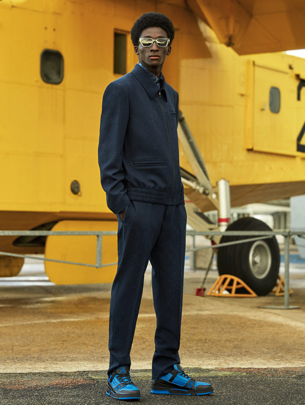 A man wearing a slick Louis Vuitton suit with blue high-top sneakers and gold sunglasses