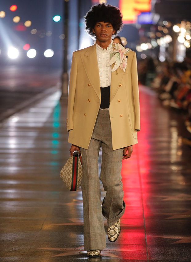 A man wearing a Gucci brown coat and checkered pants with snake skin boots