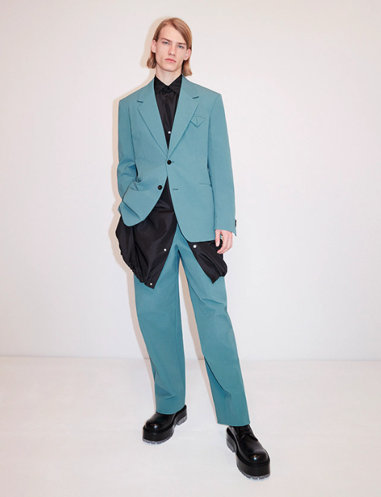 A man wearing a aqua blue suit with a blue jacket underneath along with black loafers