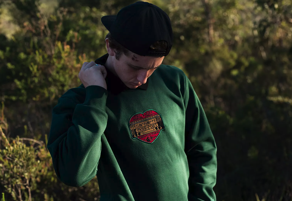 A close up of a man wearing a green Passport Skateboards hoodie with a red heart on it