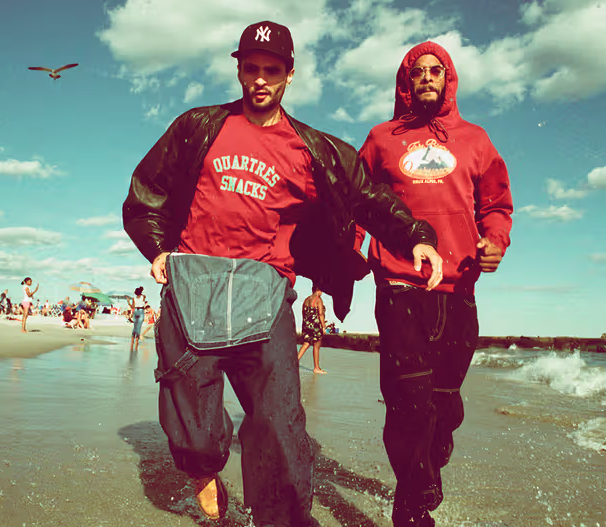 Two men walking on the beach wearing red QuarterSnacks Sweatshirts and baggy pants