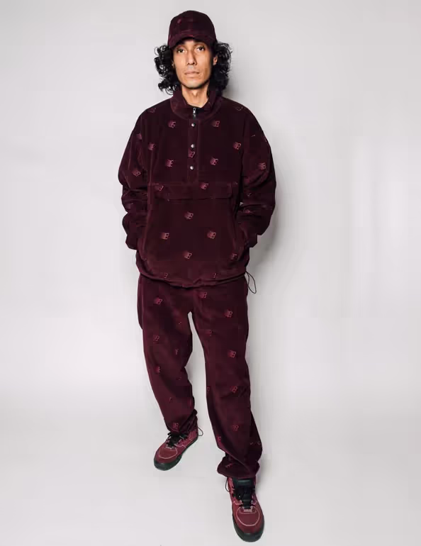 A man wearing a Bronze 56k black  fleece with matching pants and red nikes